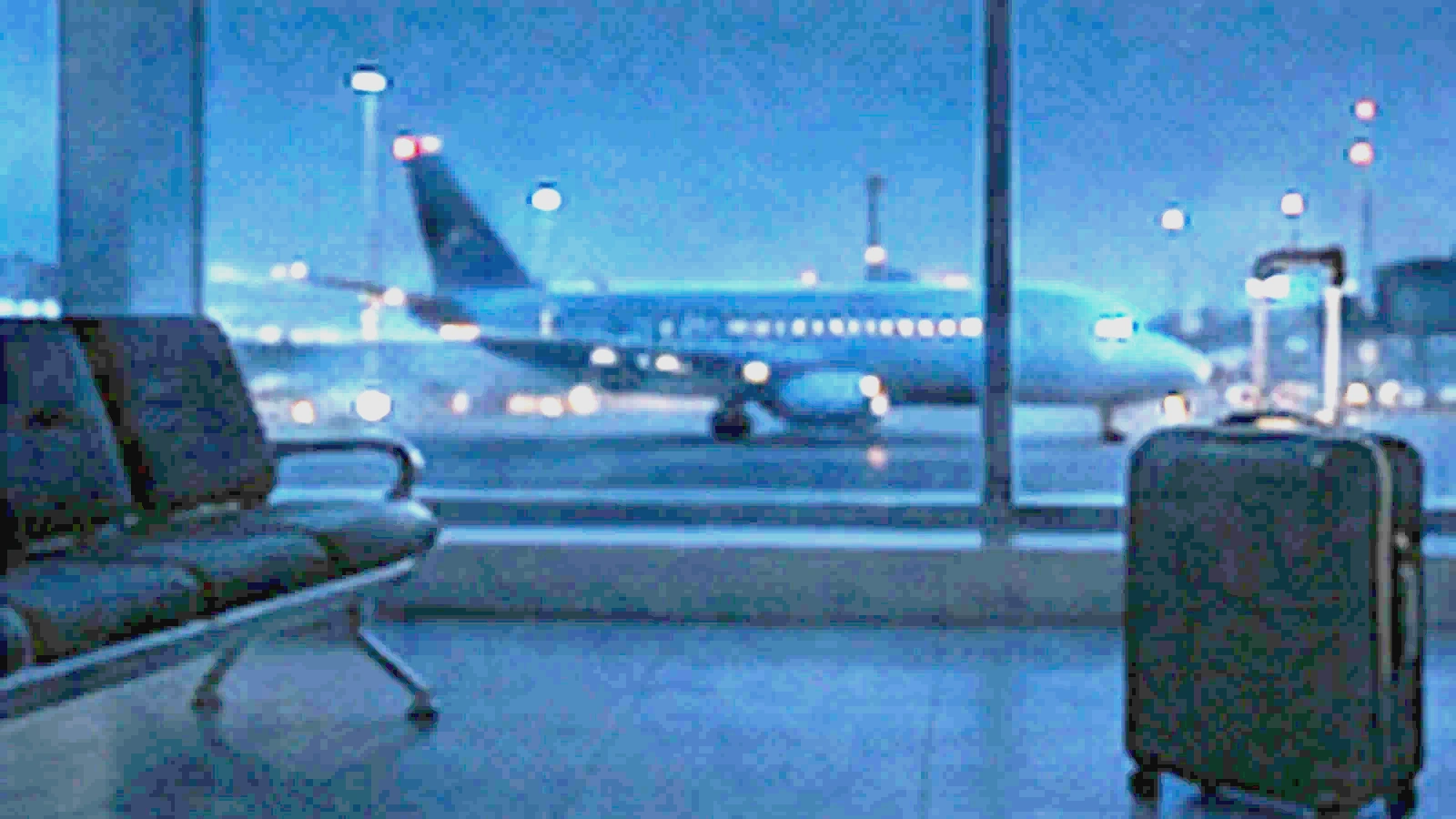 The same airport window and suitcase at night with runway lights